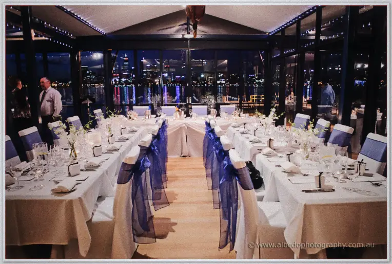 Long reception tables with navy sashes face the head table as city lights glow through the windows