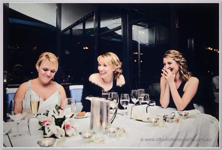 Emily and her bridesmaids laugh at the head table as speeches get under way at night