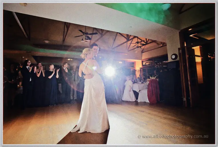 Guests applaud as backlight flares around Emily and Quentin's first dance