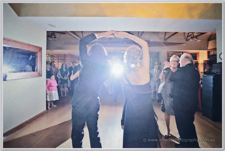 Glasses raised, wedding guests dance under a flare of light late into the reception night