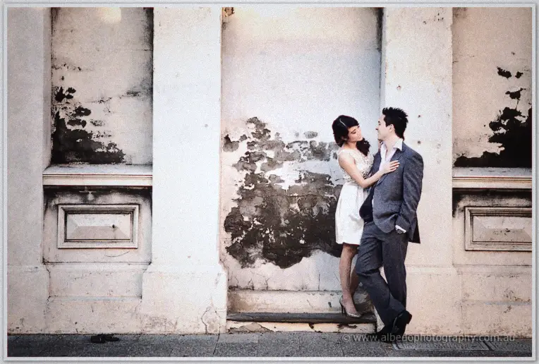 Pre wedding Fremantle | Jade and Aaron Jade tiptoes to kiss Aaron as he leans on a peeling render wall between stone columns in Fremantle