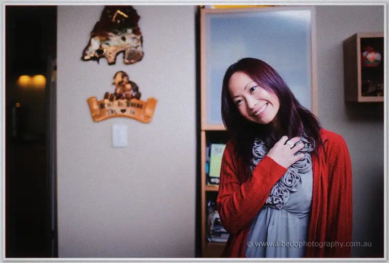 A smiling bridesmaid in a red cardigan waits in the living room during wedding morning preparations in Perth.