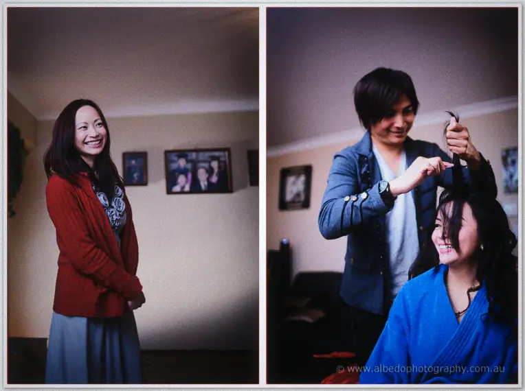 A bridesmaid in red smiles as the stylist curls Michelle's hair in a warm living room before the ceremony.
