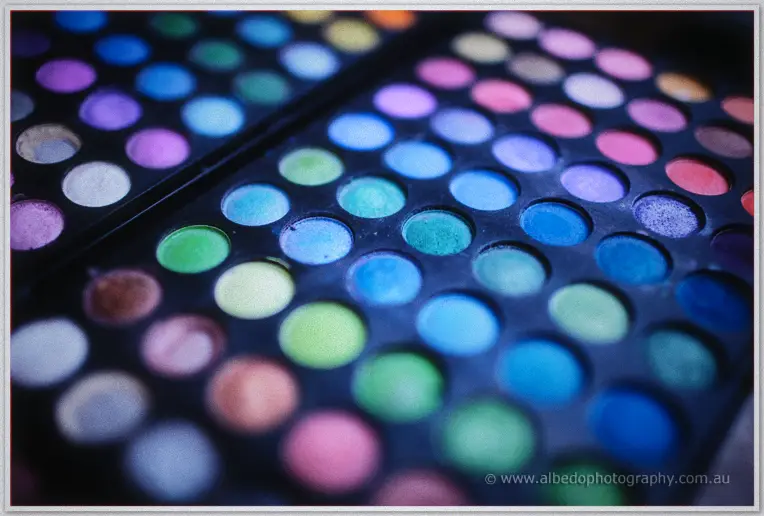 Vivid eyeshadow palettes in blues and greens wait in soft focus during Michelle's morning makeup session.