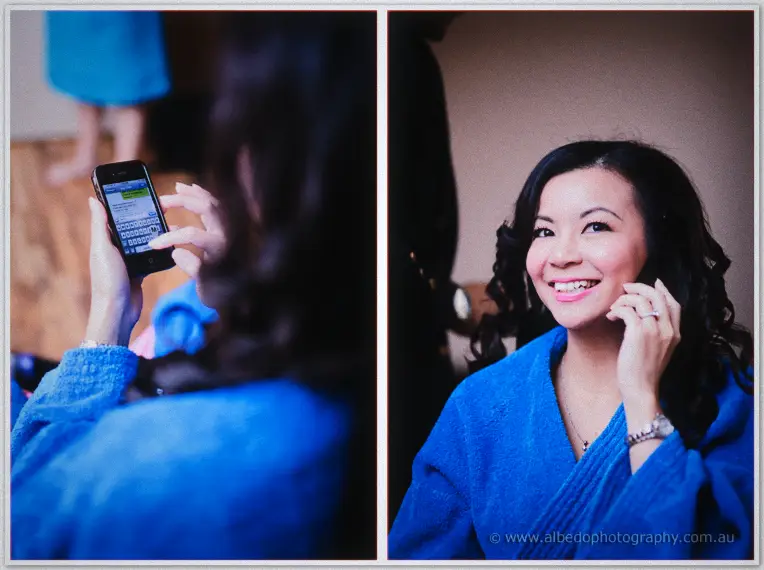 Bride Michelle in a blue robe laughs at her phone and smiles as her hair and makeup are finished at home.