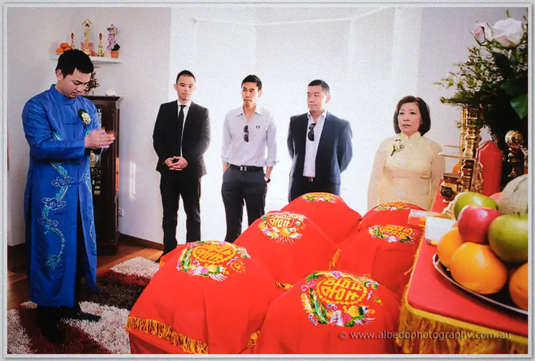 Khoa in an embroidered blue ao dai prays at the family altar before red gift trays during the tea ceremony.