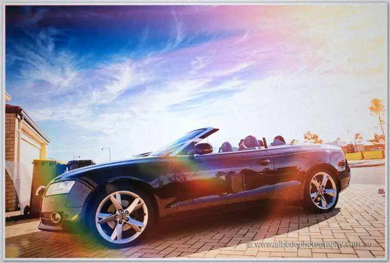 A black convertible wedding car gleams on the paver driveway under a bright, sun-streaked Perth sky.