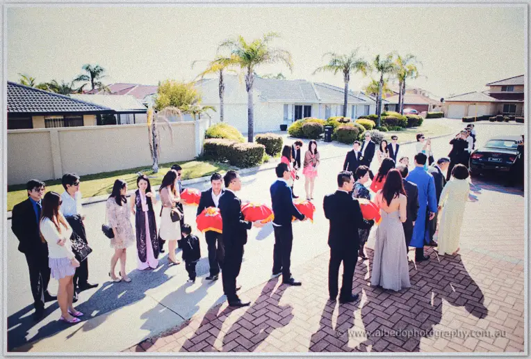 The wedding procession gathers on a suburban Perth street, red gift trays and palm trees in view.