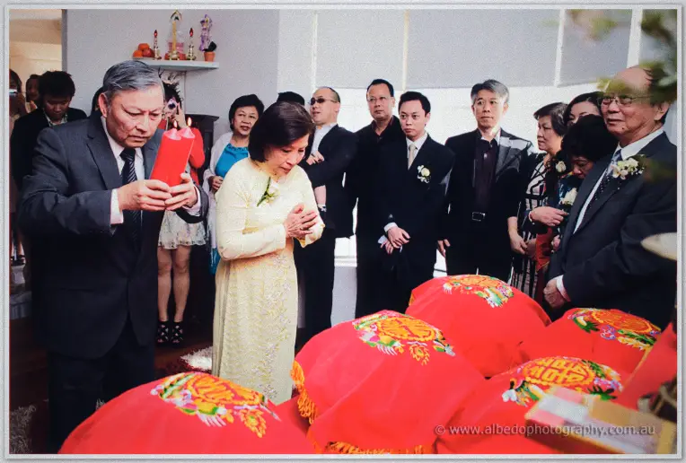 Khoa's father lights red ceremonial candles as his mother prays before the gift trays.