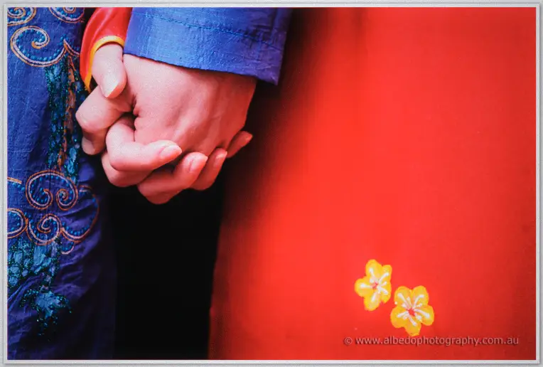 Close-up of Michelle and Khoa's clasped hands against the red and blue silk of their ao dai.