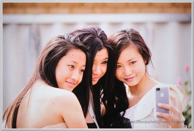 Three young guests squeeze together for a playful selfie in the sunshine during the wedding celebrations.