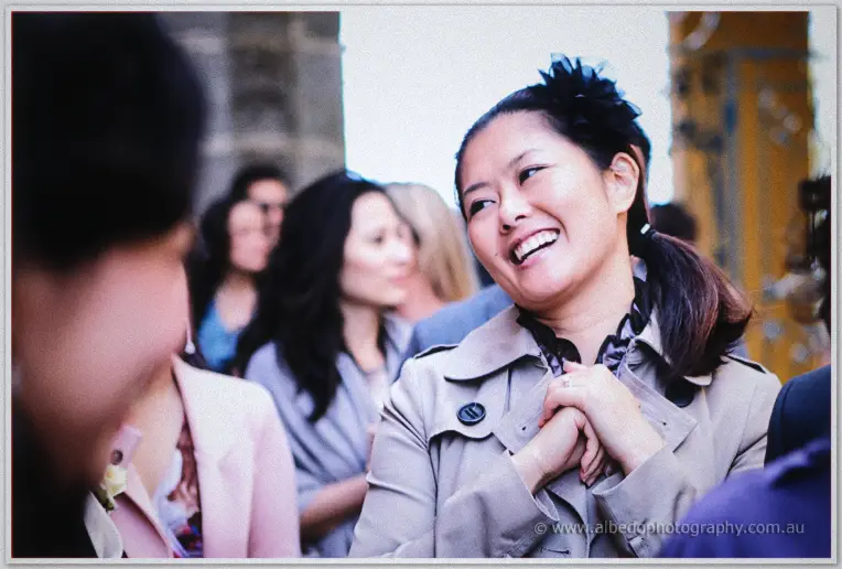 A laughing guest in a trench coat and black feathered hairpiece mingles outside after the service.