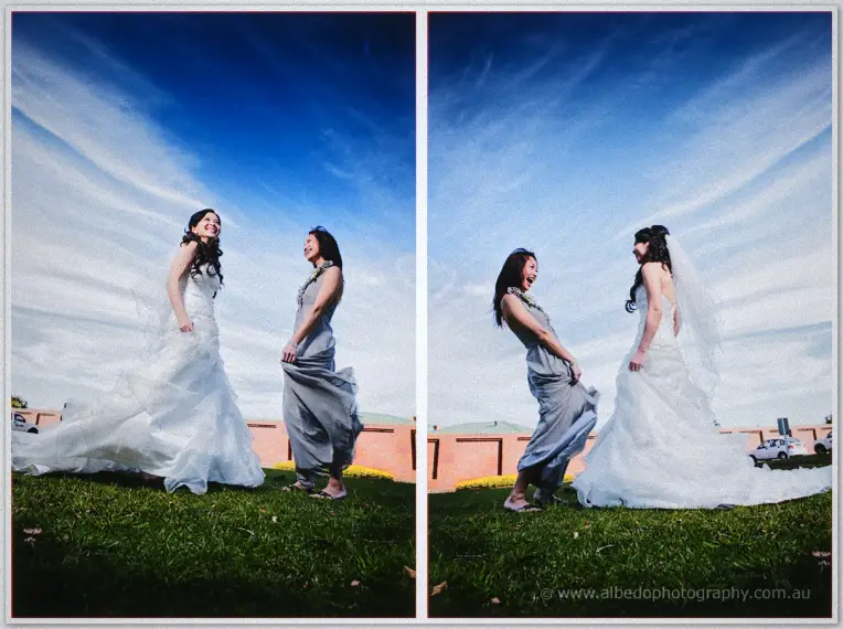 A bridesmaid in grey poses beside Michelle in the stone corridor, arm linked warmly.