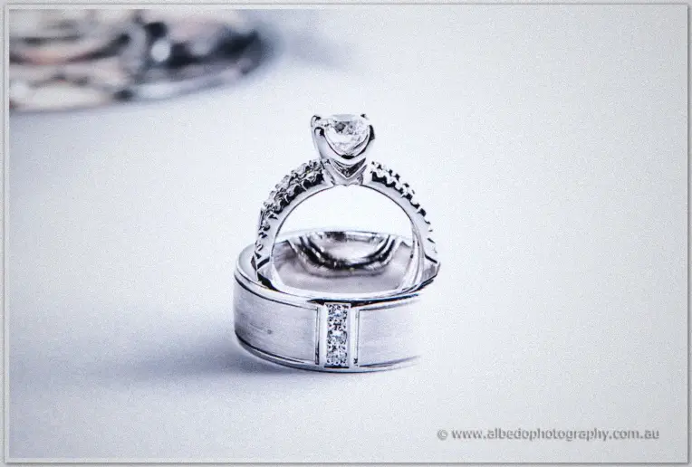 Close-up of Michelle's diamond engagement ring balanced on Khoa's engraved wedding band in soft window light.