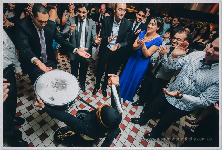 Guests in suits and blue gowns sway around the kneeling drummer on the chequered dance floor