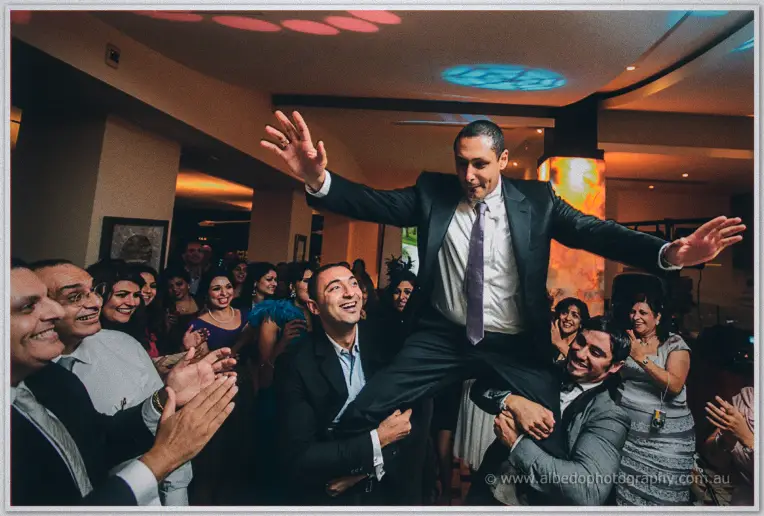 Friends hoist Mina onto their shoulders, his arms flung wide over the packed dance floor