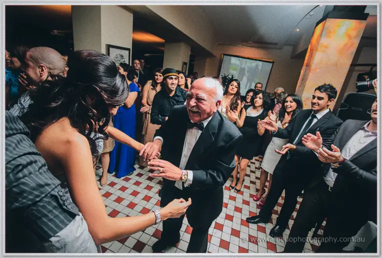 Lydia shares a laughing dance with a white-haired elder in a bow tie as guests applaud