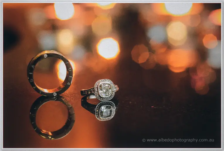 His engraved dark band and her diamond halo ring catch the golden glow of city lights