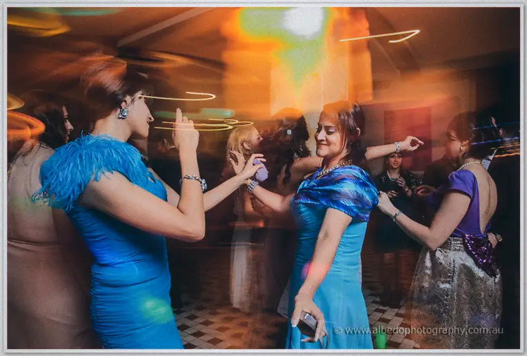 Guests in vivid blue gowns sway beneath streaks of party light on the dance floor