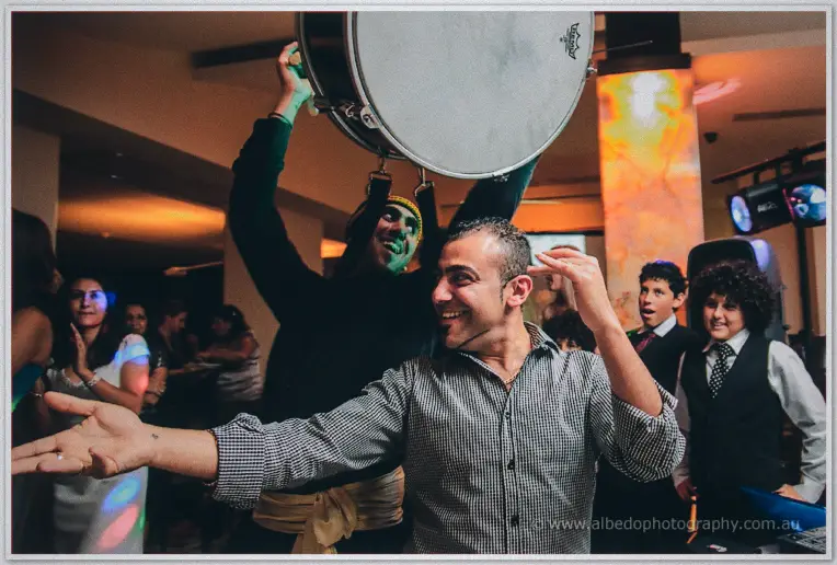 A grinning guest dances arms wide while the drummer hoists his bass drum overhead