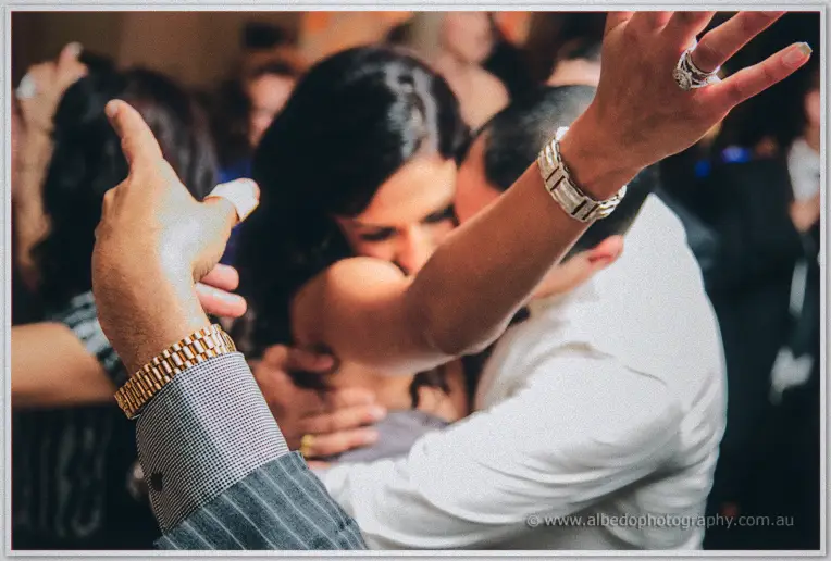 Lydia and Mina embrace on a packed dance floor as guests raise ringed hands in celebration