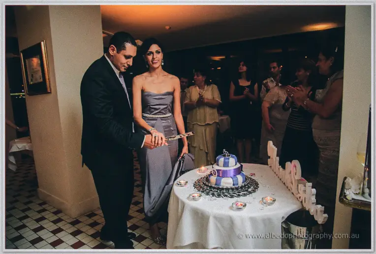 Lydia and Mina cut their blue and white engagement cake as guests applaud around them
