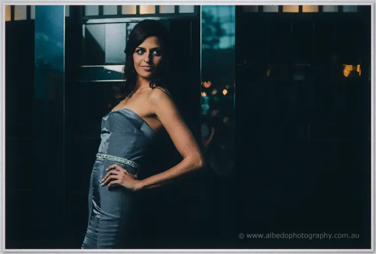 Lydia glances back over her bare shoulder in a beaded grey gown against dusk-lit hotel glass
