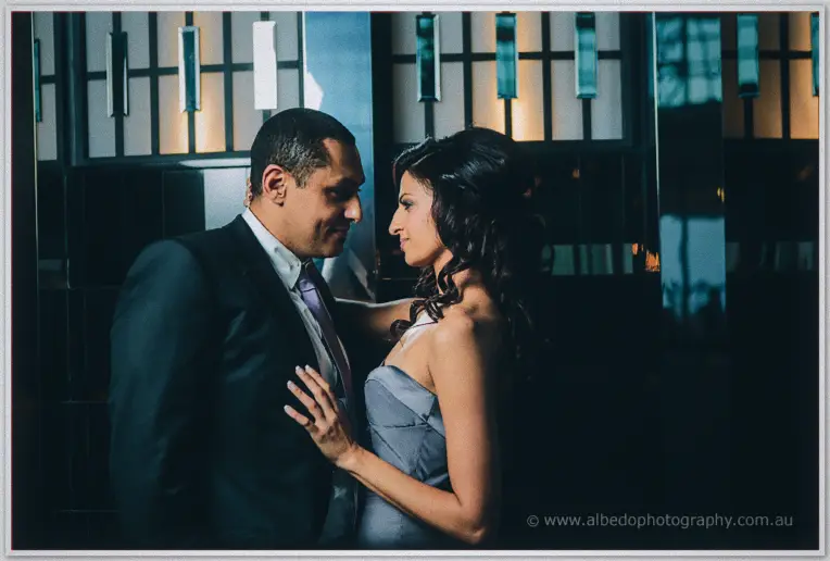 Face to face in the teal-lit lobby, Lydia rests a hand on Mina's chest as they lean close