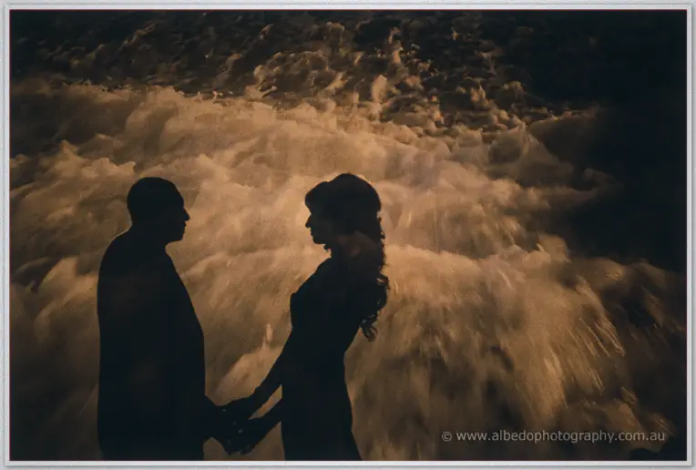Hand in hand at the water's edge, the couple stands silhouetted against golden rushing surf