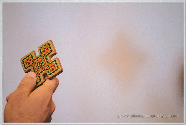 A hand lifts an embroidered wooden cross aloft against the plain wall of the church