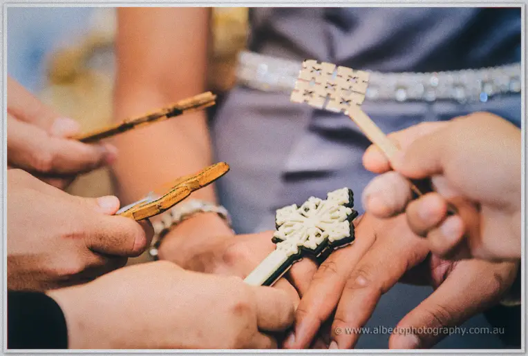 Family members hold small wooden crosses over the couple's clasped hands in blessing
