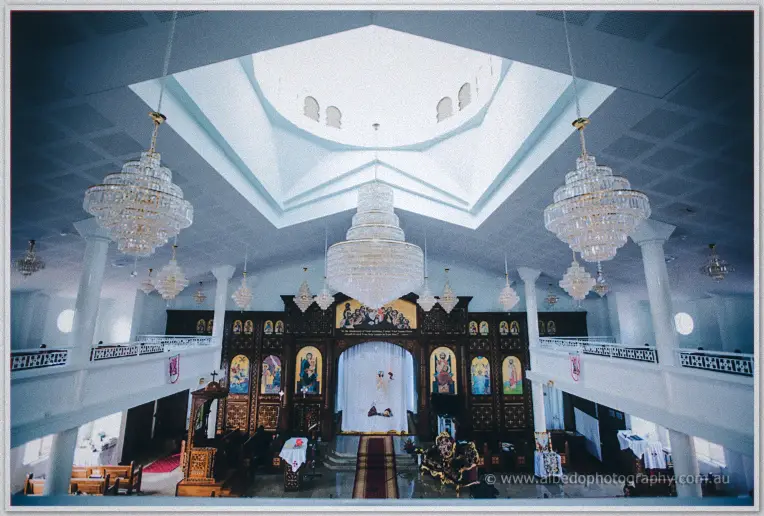 Crystal chandeliers hang over the icon-adorned sanctuary of a white Coptic Orthodox church