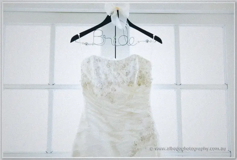 Sarah's beaded lace gown glows on its hanger against soft window light at Brookleigh.