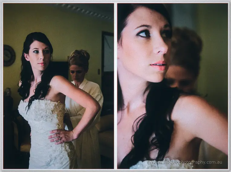 A woman in a white robe adjusts Sarah's gown as she steals a nervous sideways glance in dim light.