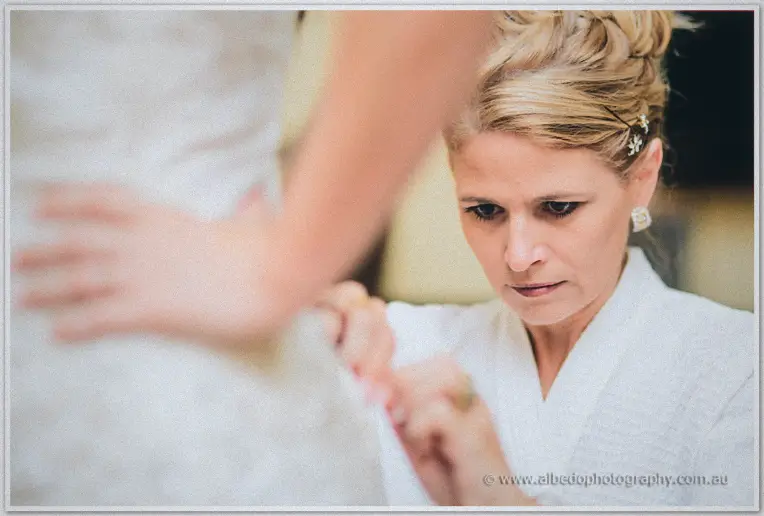 In tight profile, an older woman concentrates on fastening the back of Sarah's lace gown.