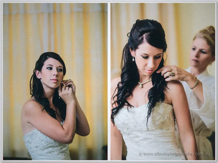 Sarah fastens an earring, then a woman in white drapes a pearl necklace over her lace gown.