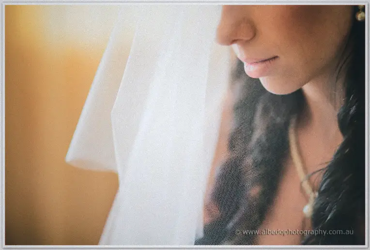 Soft close-up of Sarah's lips and dark curls behind a sheer veil in warm golden morning light.