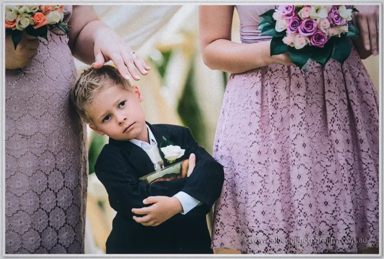 Pageboy hugs the ring box to his chest while a bridesmaid rests a hand on his hair near the altar.
