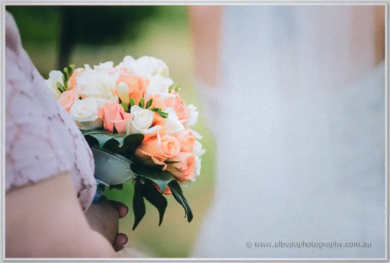 Close-up of peach and cream roses against the soft blur of a bride's gown in the background.