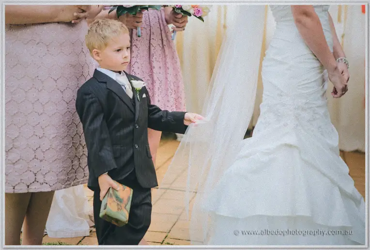 Pageboy in pinstripe reaches for the bride's trailing veil on the pavilion's brick floor.