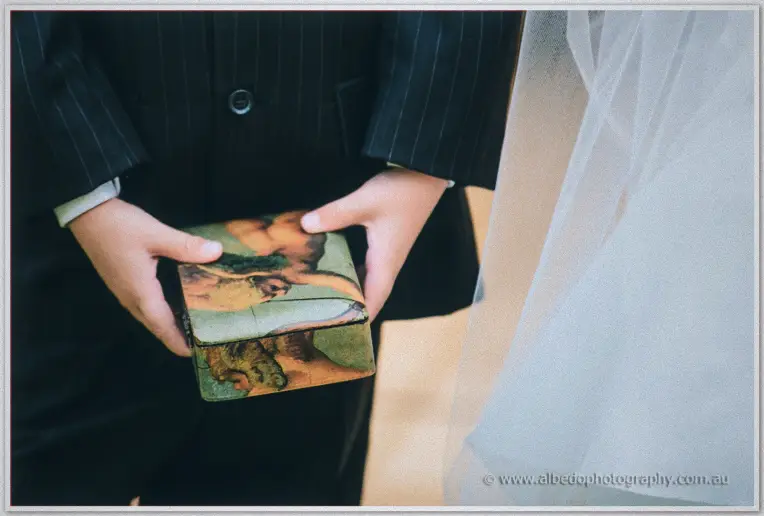 Small hands cup a painted keepsake box as the bride's veil drifts past the boy's dark suit.