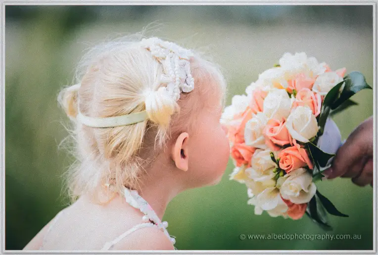 Little girl in pearl headband leans in to sniff a peach and cream rose bunch held out to her.