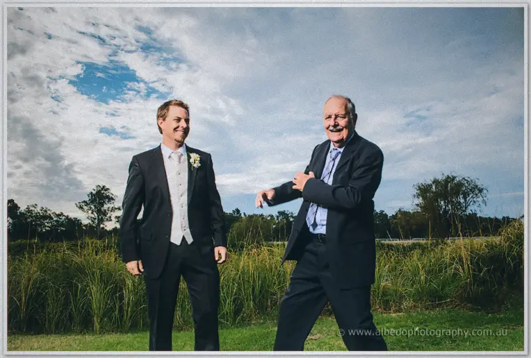 Daniel grins beside an older gentleman in a navy suit under a dramatic sky in the Brookleigh grounds.