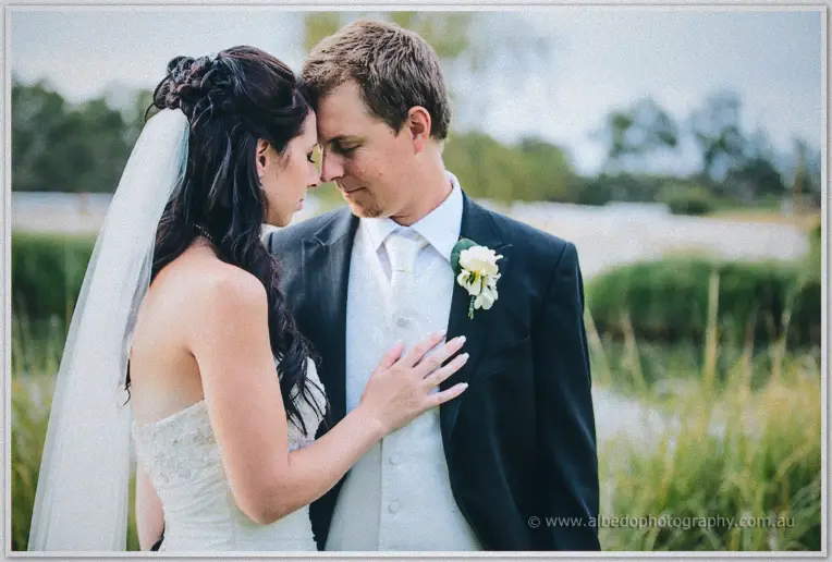 Sarah and Daniel touch foreheads by the water at Brookleigh, her hand resting on his lapel.