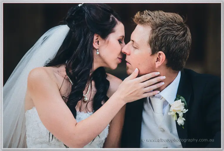 Sarah cups Daniel's cheek as the two share a quiet kiss against a dark rustic wall.