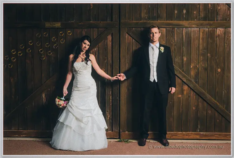 Sarah and Daniel hold hands before the rustic barn doors, her bouquet swinging at her side.