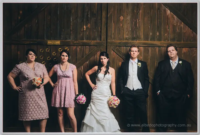 Bridal party strikes a posed line against the weathered timber doors of the Brookleigh barn.