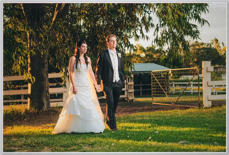 Golden-hour light warms Sarah and Daniel as they stroll past the paddock fence at Brookleigh.