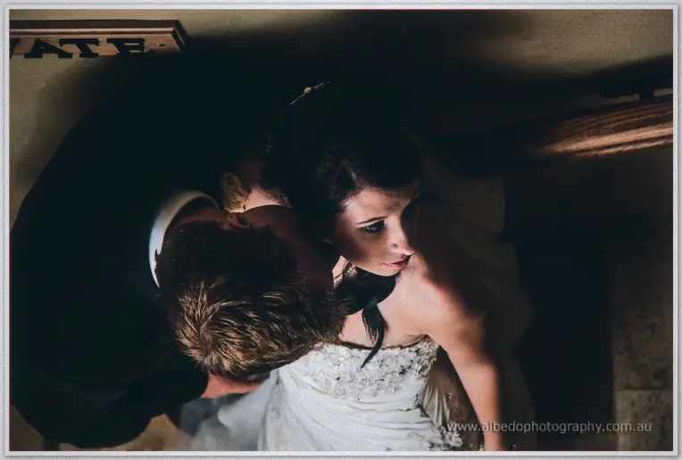 From above, Daniel presses a kiss to Sarah's shoulder in a dim timber-beamed room at Brookleigh.