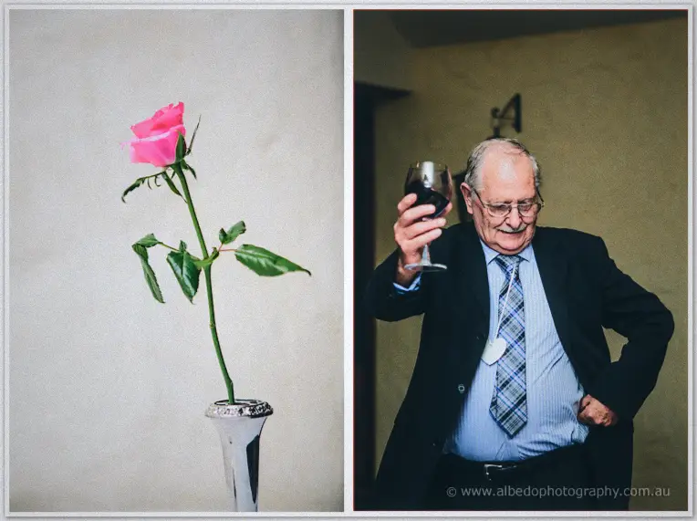 A pink rose leans from a silver bud vase beside an older guest raising his red wine in toast.